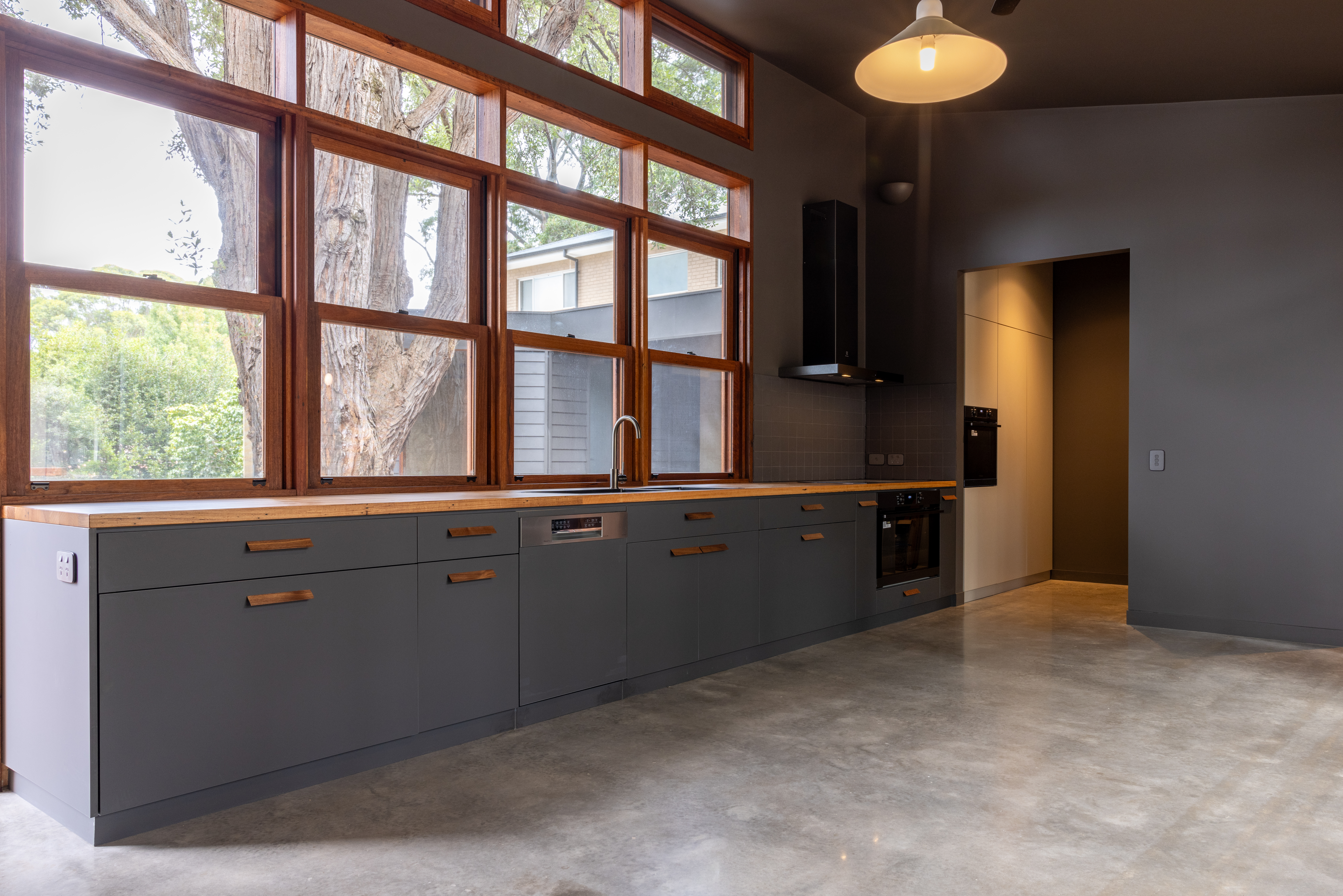 Kitchen — dark cabinetry with timber handles, hardwood benchtop and full-height windows