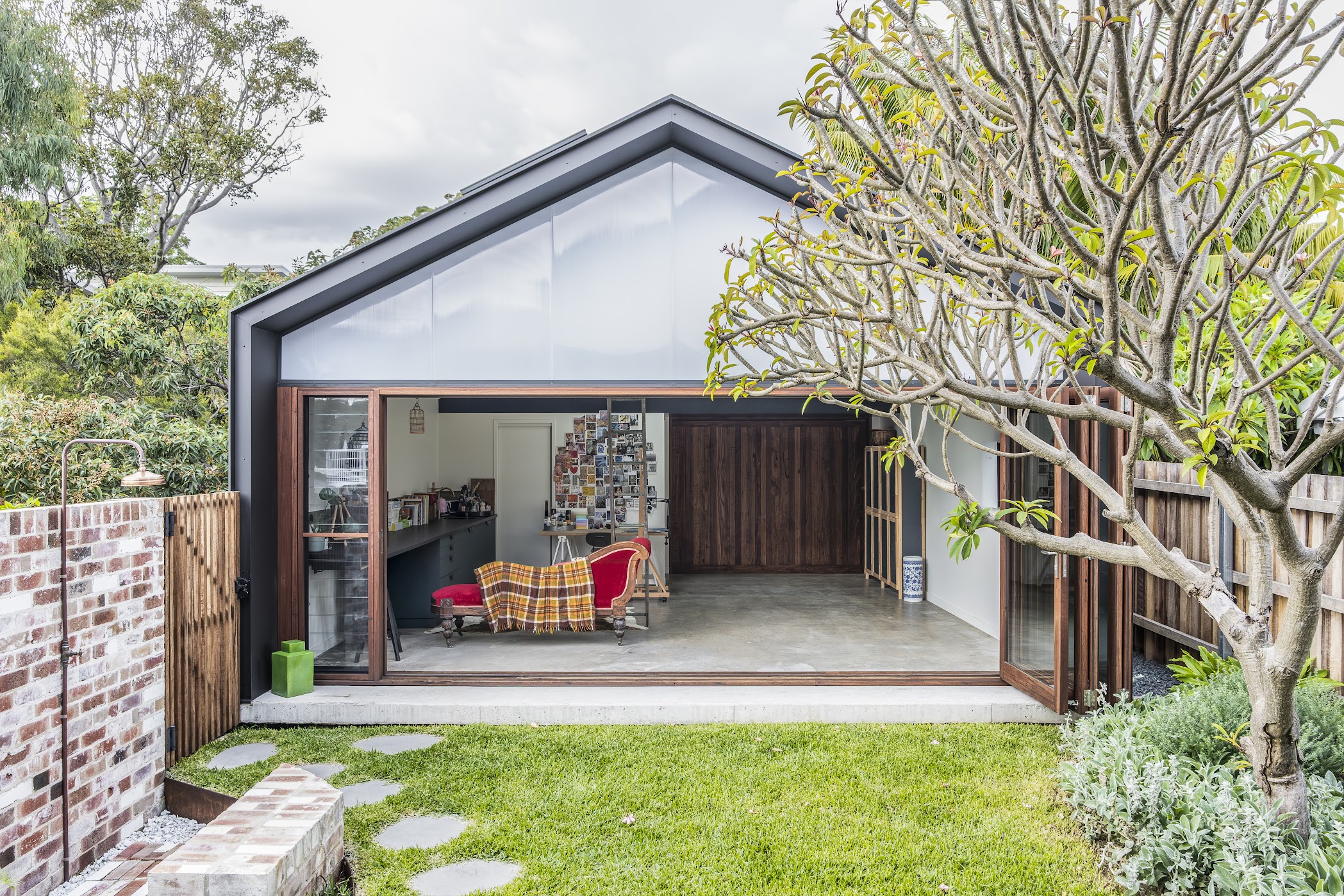 Studio pavilion — gabled polycarbonate roof, dark steel frame, bifold doors open to garden