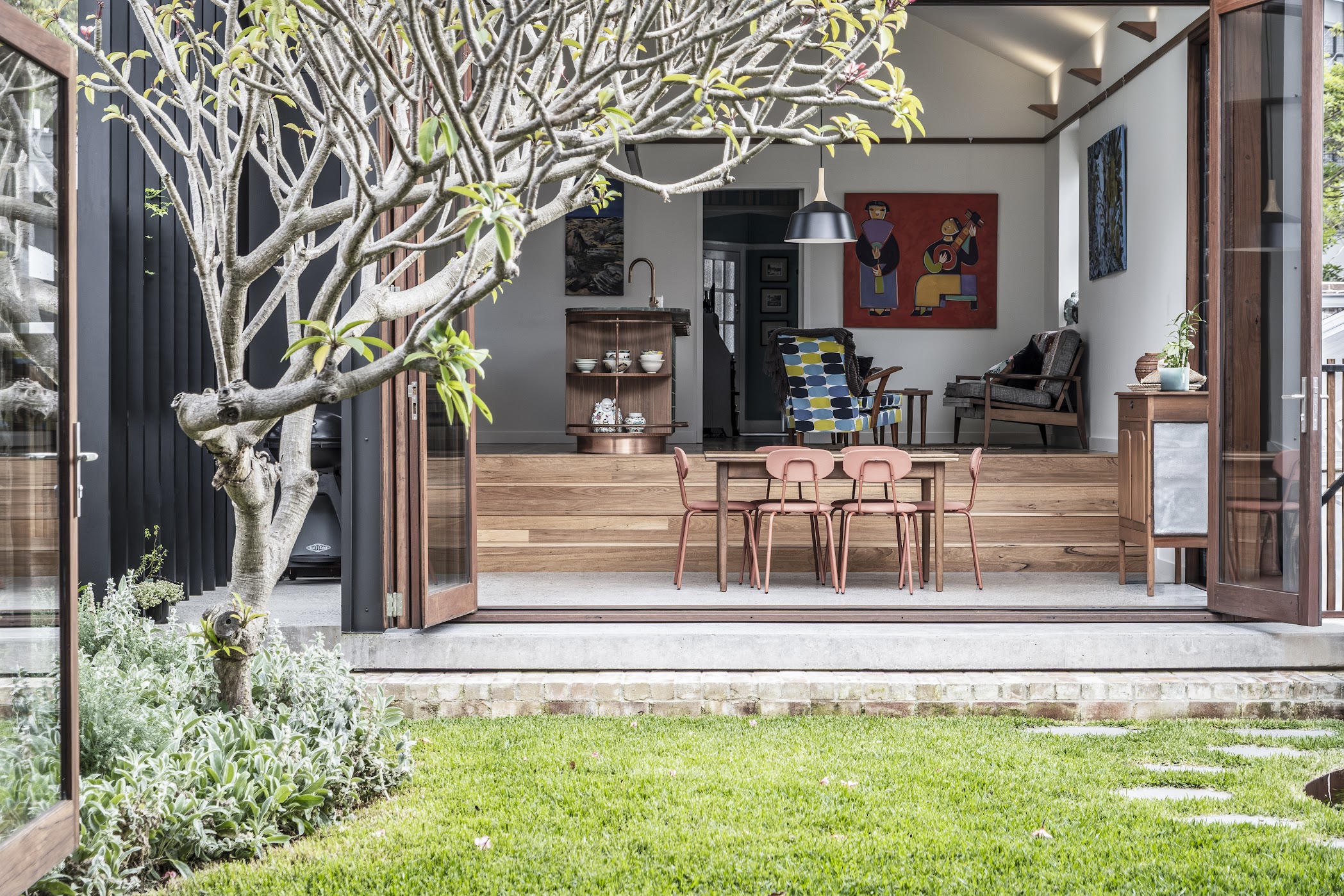 Courtyard dining — frangipani tree, pink dining chairs, open living pavilion beyond