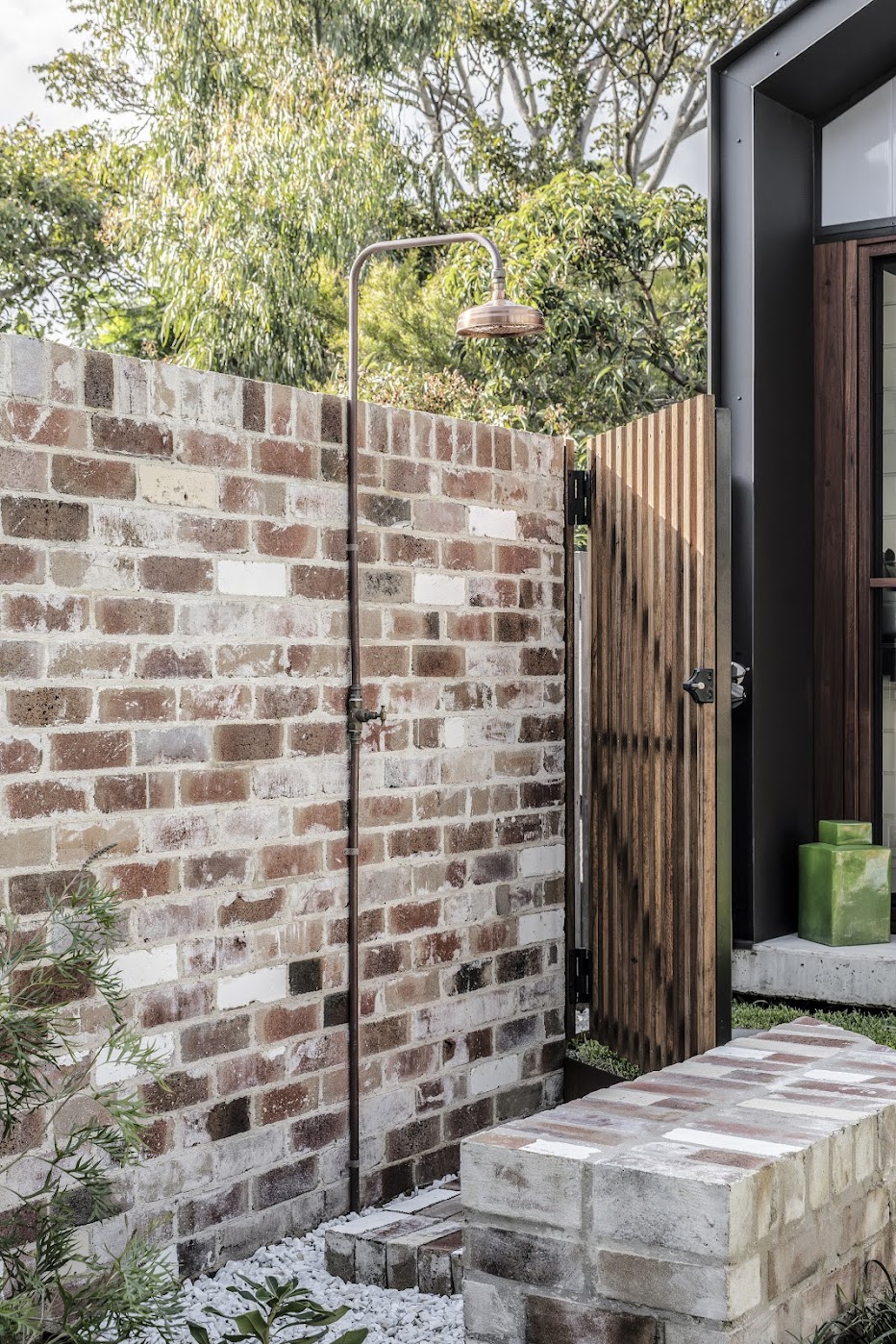 Outdoor shower — copper shower rose against recycled brick wall with timber gate